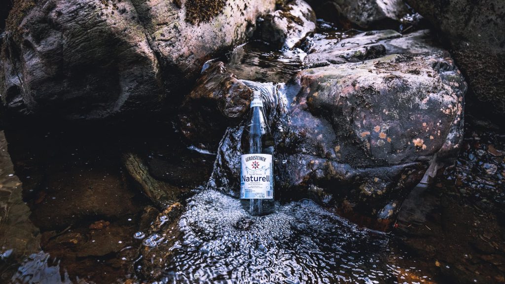 Eine Flasche Gerolsteiner Naturelle, präsentiert im Bachlauf eines Flusses.