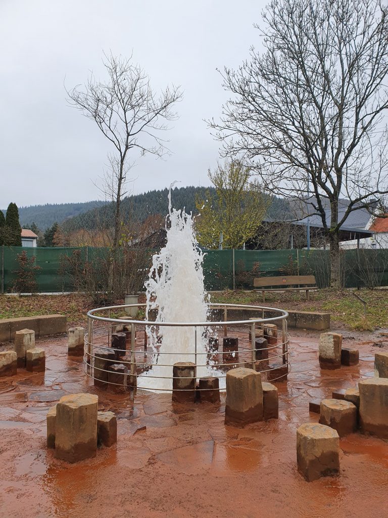 Kaltwasser-Geysir in Wallenborn. Die Erde rundherum ist aufgrund des Eisengehalts orange verfärbt. 