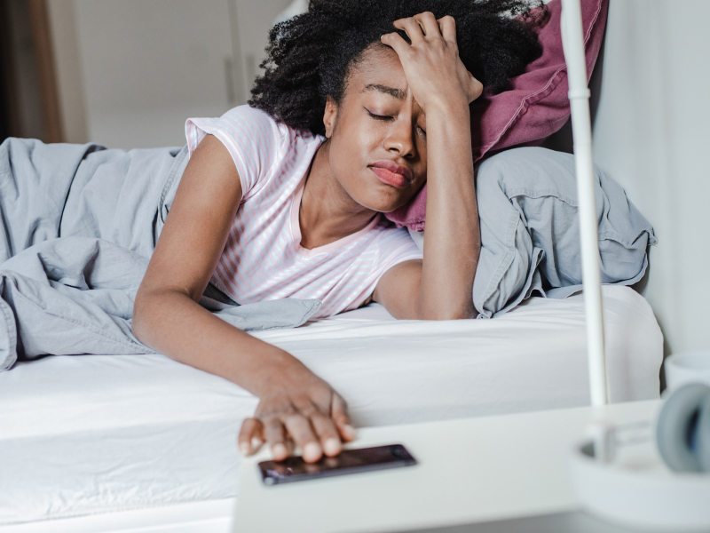 Eine Frau liegt mit Kopfschmerzen im Bett.