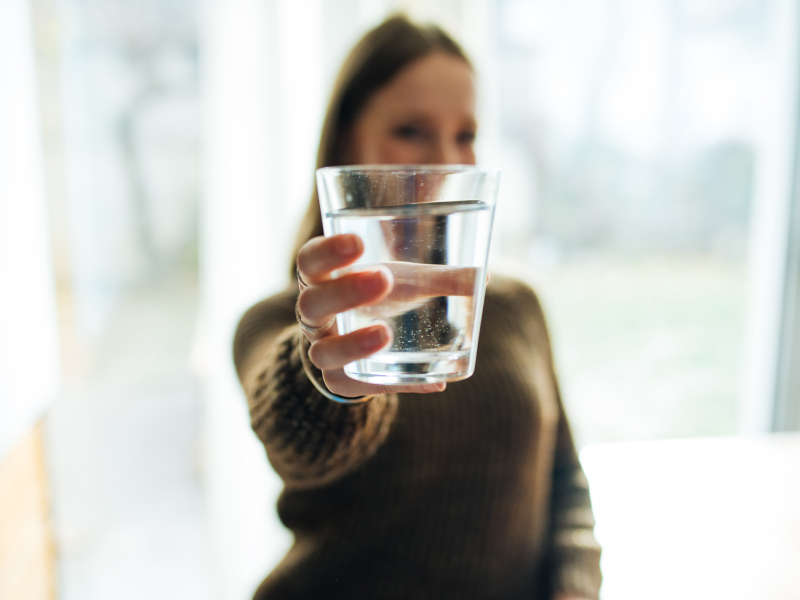 Eine Frau reicht ein Glas Wasser in Richtung Kamera.