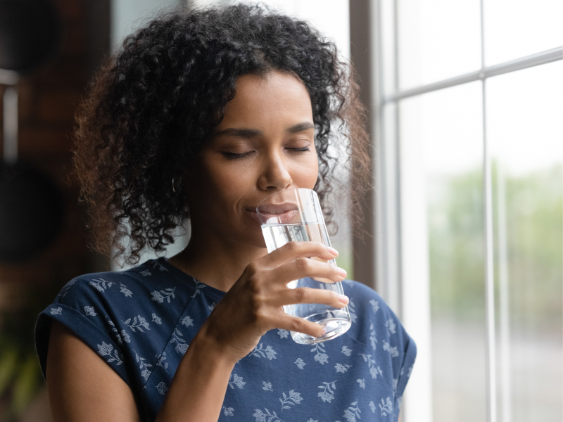 Eine Frau trinkt ein Glas Wasser und hat dabei die Augen geschlossen.