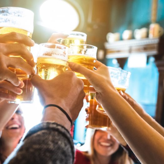 Personen halten Gläser mit Bier in die Luft und stoßen an.