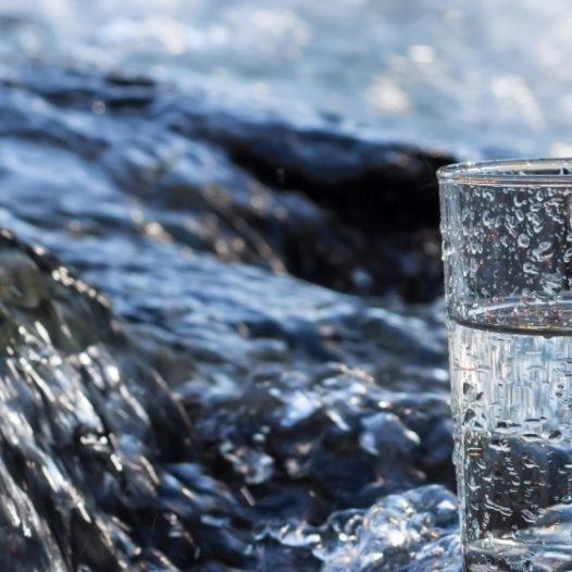 Fluss/Bach und Glas mit Wasser im Vordergrund.
