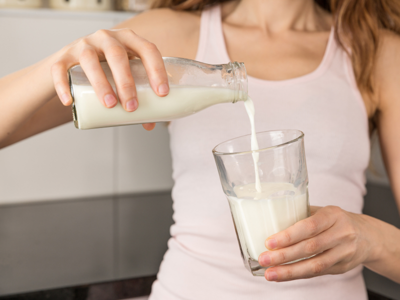 Eine Frau gießt Milch aus einer Flasche in ein Glas.