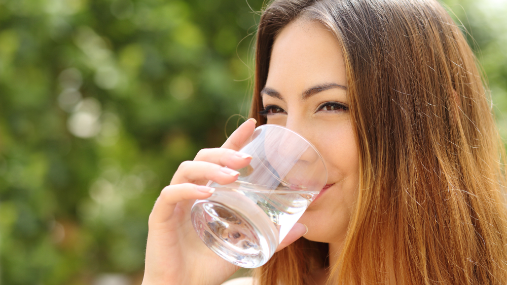 Eine Frau trinkt Mineralwasser aus einem Glas.