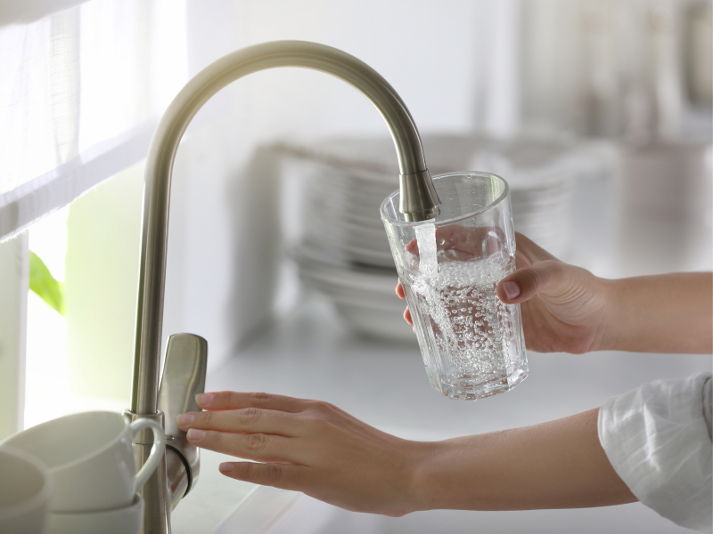 Eine Frau lässt Leitungswasser in ein Glas laufen.