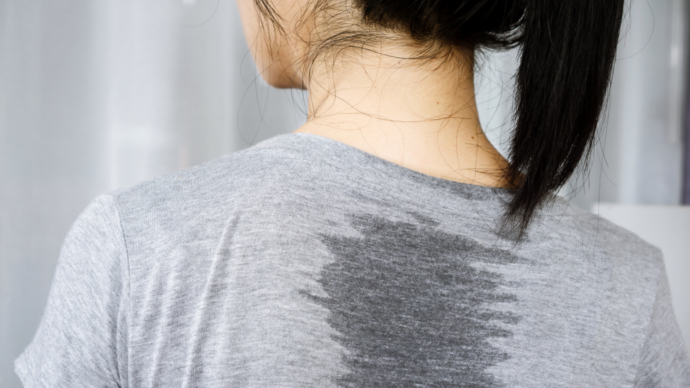 Frau mit einem Schweißfleck auf dem T-Shirt.