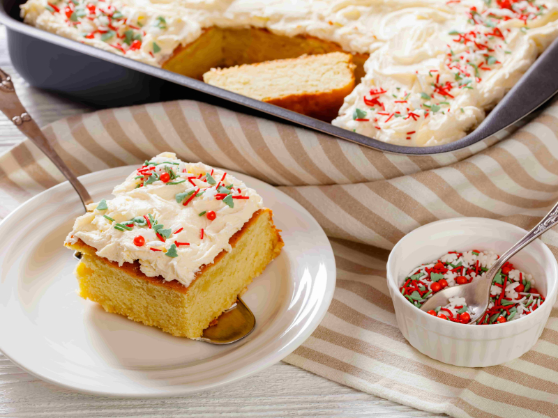 Heller Blechkuchen mit Zuckerguss und Streuseln. Im Vordergrund liegt ein Stück Kuchen bereits auf dem Teller. Die übrigen Streusel stehen daneben in einer kleinen Schale. Im Hintergrund ist der restliche Kuchen noch auf dem Blech.