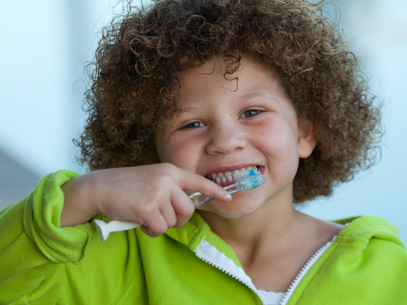 Kleines Kind mit stark lockigen, braunen Haaren putzt sich die Zähne.