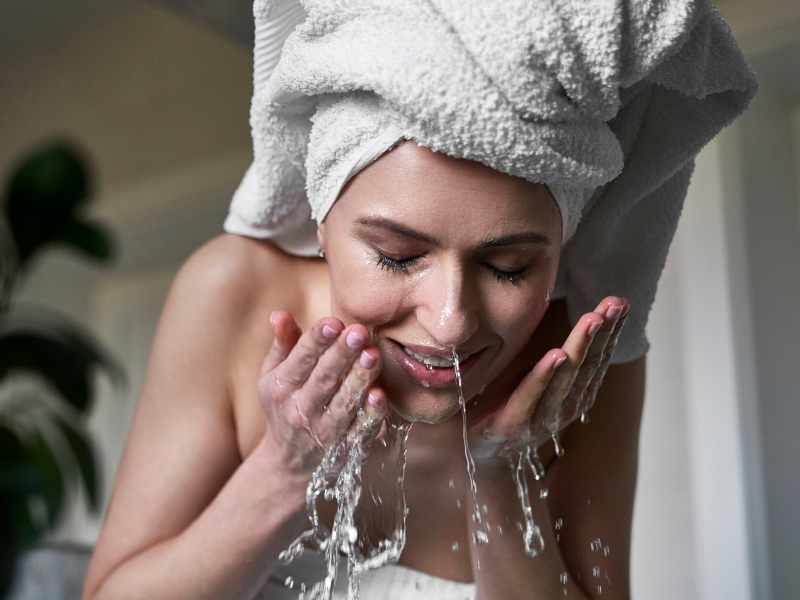 Vorderansicht einer Frau, die im Badezimmer ihr Gesicht mit Wasser wäscht.