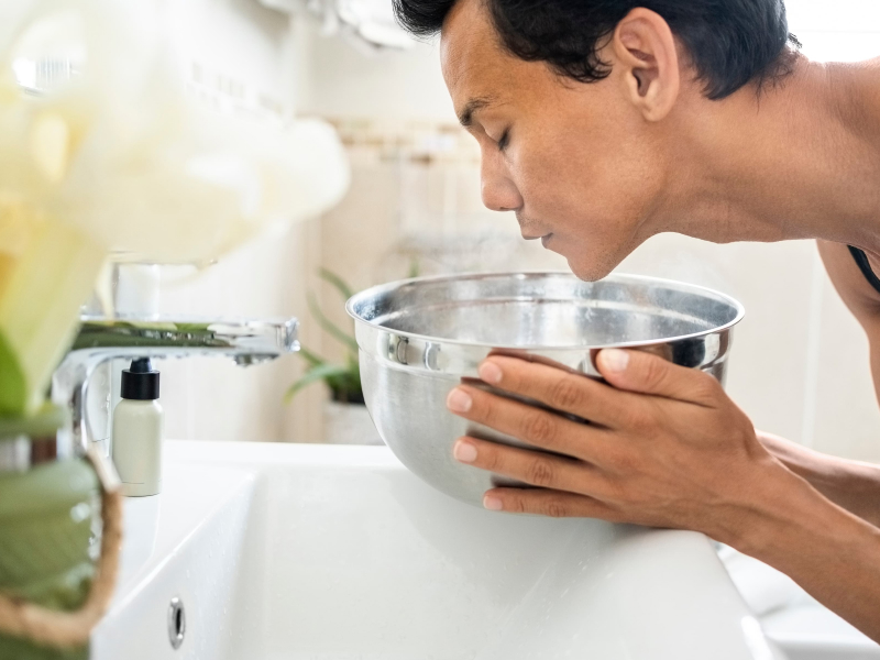 Ein Mann hält sein Gesicht über einer silbernen Schüssel mit Wasser.