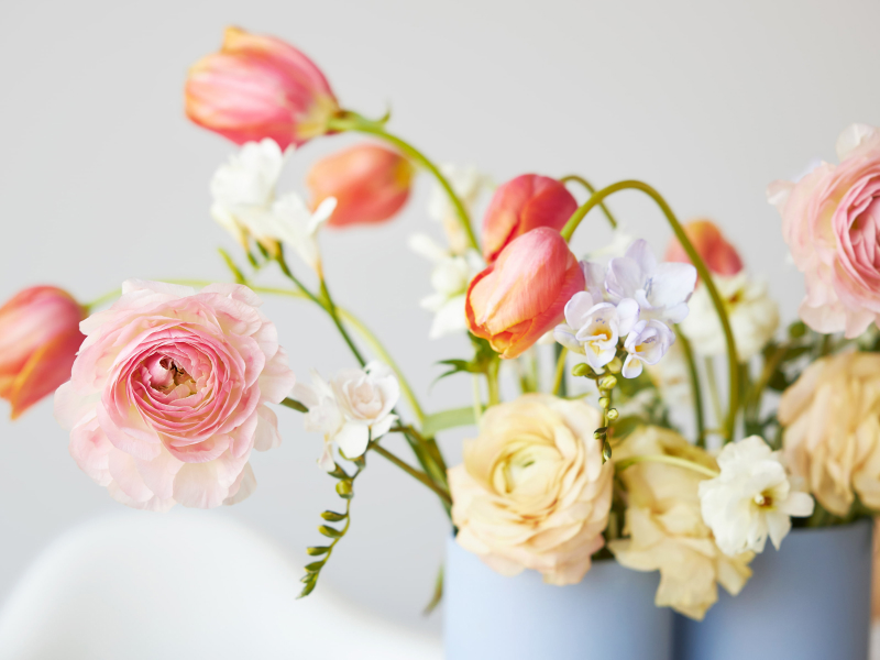 Ein moderner Frühlingsstrauß aus Freesien, Ranunkeln und Tulpen in einer schönen Vase auf einem Esstisch