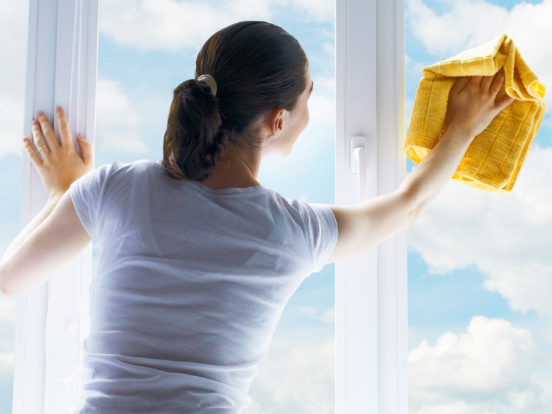 Eine Frau putzt mit einem Lappen die Fenster. 