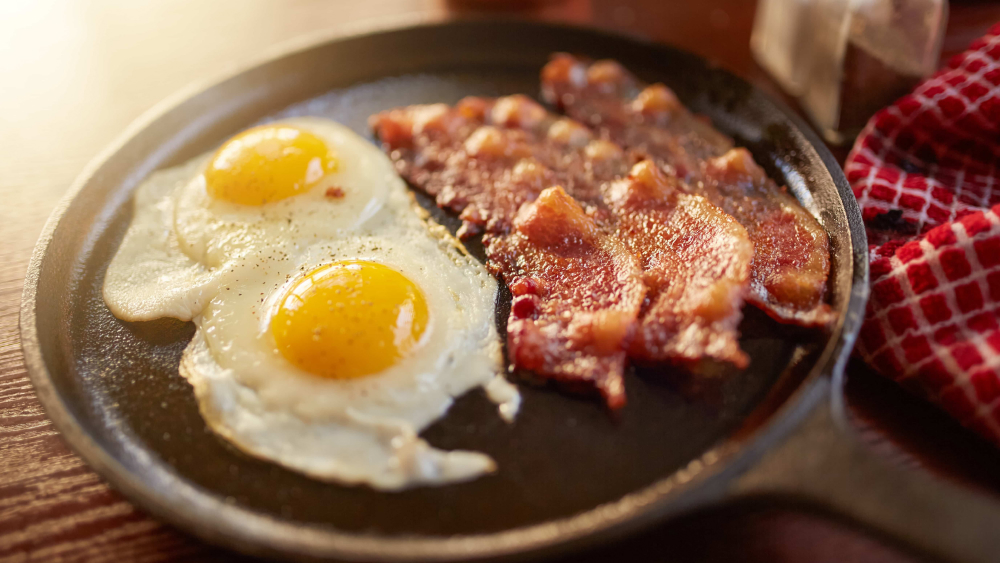 2 Spiegeleier und 3 Streifen Bacon in einer Pfanne mit Wasser gebraten.