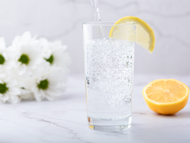 Erfrischendes Mineralwasser mit Kohlensäure wird in ein Glas mit einer Zitronenscheibe gegossen.