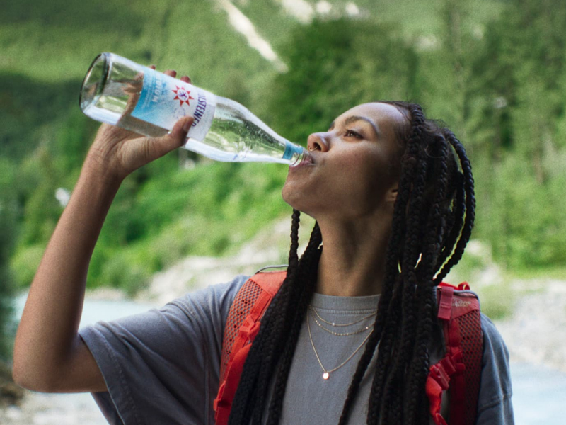Eine junge Frau trinkt Mineralwasser aus einer Flasche Gerolsteiner Medium während dem Sport.
