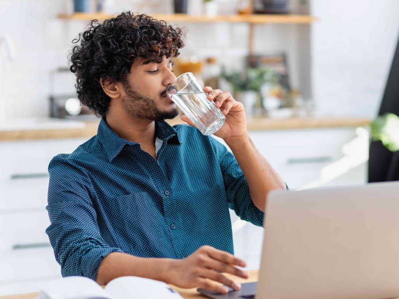 Ein Mann sitzt am Laptop und trinkt ein Glas Wasser.