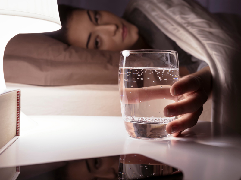 Frau trinkt vorm Schlafen ein Glas Wasser.