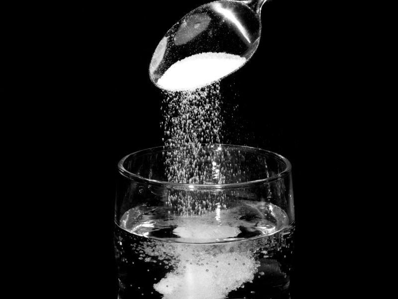 Von einem silbernen Löffel rieselt Salz in ein Glas mit Wasser.