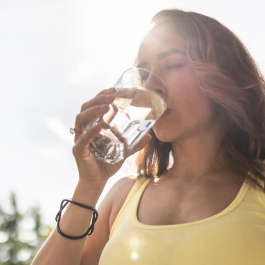 Eine Frau steht draußen in der Sonne und trinkt Mineralwasser, eine natürliche Zinkquelle.