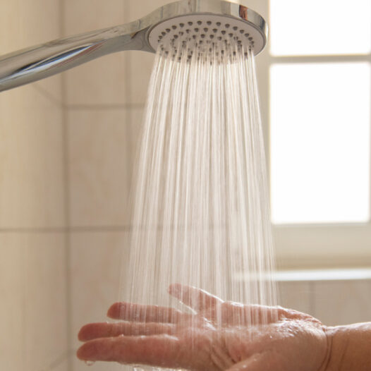 Hand unter einem Wasserstrahl aus einem Duschkopf.