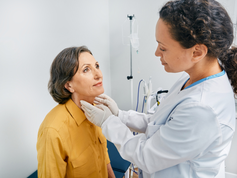 Ärztin tastet den Hals ihrer Patientin ab und untersucht die Schilddrüse.