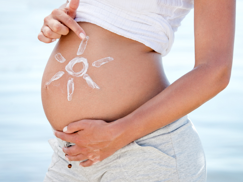 Schwangere Frau hat mit Sonnencreme eine Sonne auf ihren Bauch gecremt.