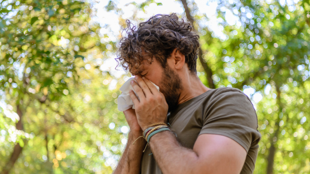 Mann mit Heuschupfen niest in ein Taschentuch