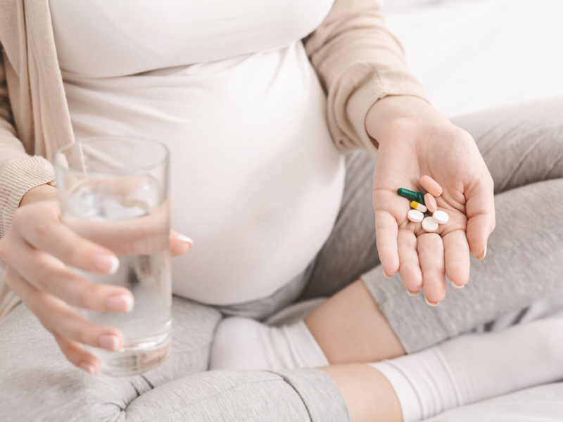 Schwangere Frau hält ein Glas Wasser und Supplements in der Hand