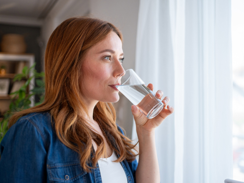 Frau trinkt nach ersten Migräne Anzeichen ein Glas Wasser